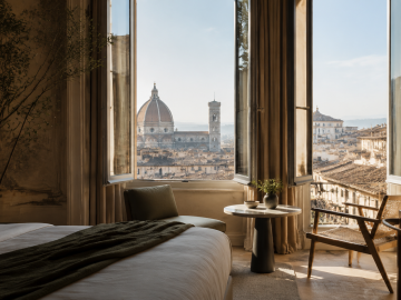 Luxury hotel room overlooking Florence Cathedral through open windows in the morning light.